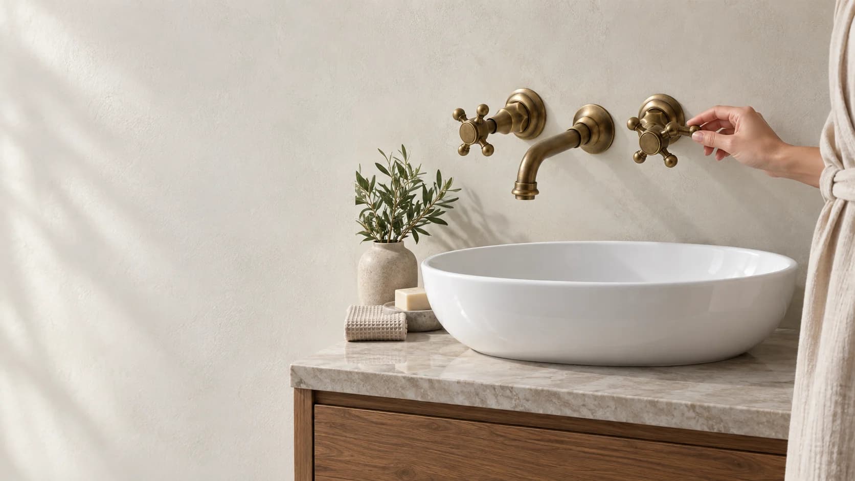 Rubinetto bagno rustico a parete sopra un lavabo montato su un mobile; una persona di lato controlla la maniglia con l’acqua chiusa.